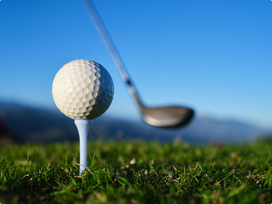 Pelota sobre el tee en un campo de golf, con un palo desenfocado al fondo lista para el golpe