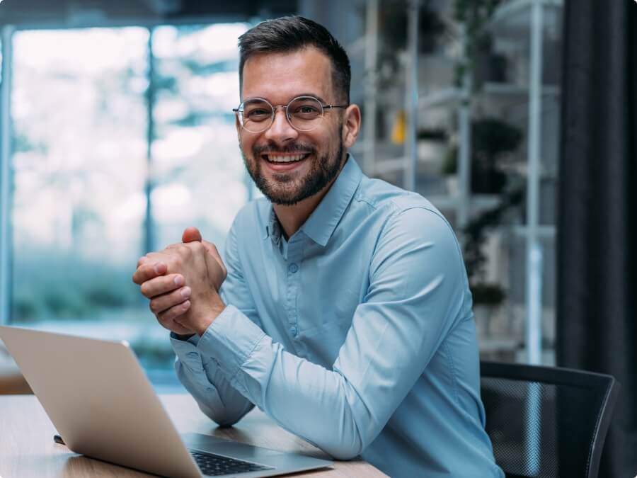 Hombre sonriendo frente a una notebook, con las dos manos juntas