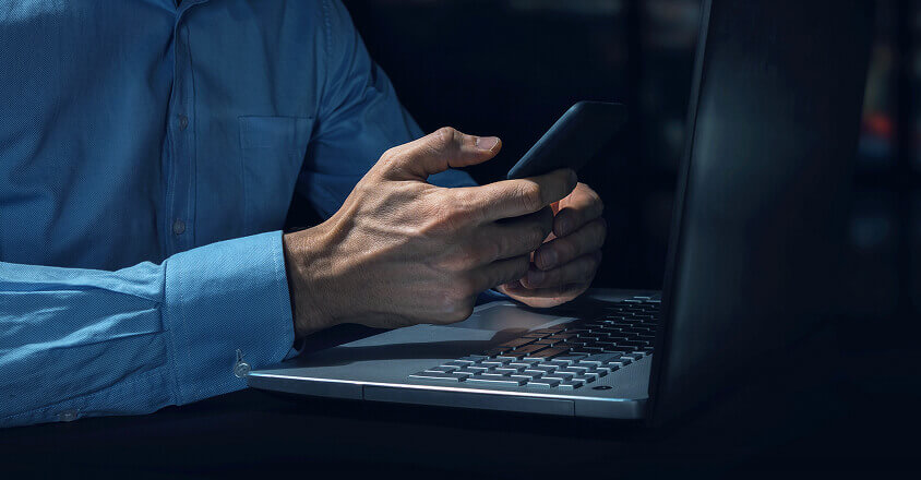 Mano sosteniendo un celular y usando una computadora