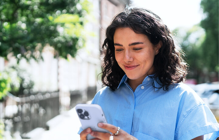 Chica sonriendo, sosteniendo y mirando el celular en un ambiente al aire libre