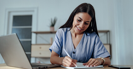 Empresaria sonriendo y tomando notas en una tablet, con una notebook al frente