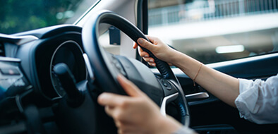 Volante de un auto en movimiento en primer plano, con las manos de una mujer sujetándolo con ambas manos