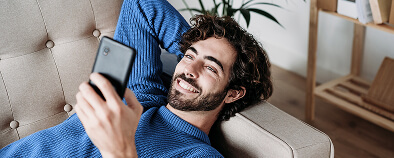 Joven recostado en el sofá, sonriendo y mirando la pantalla del celular