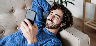 Joven recostado en el sofá, sonriendo y mirando la pantalla del celular
